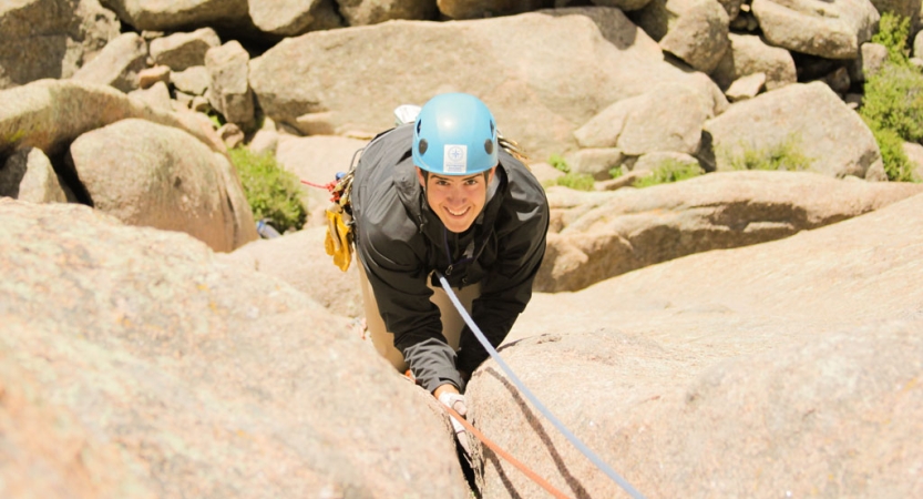 a person wearing safety gear looks up and smiles while rock climbing